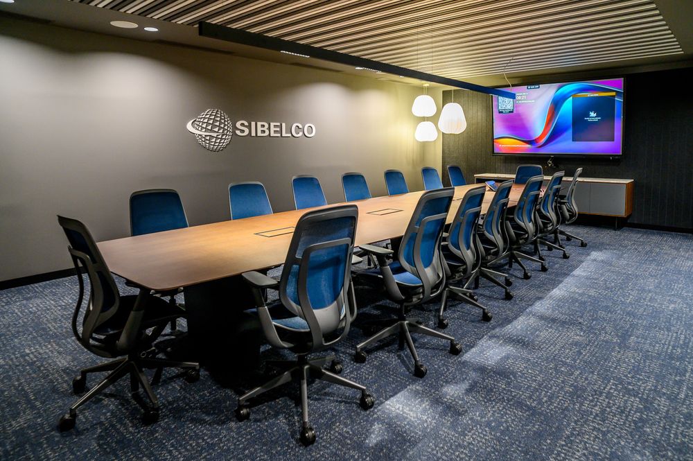 Sala de reuniones con gran mesa de madera, sillas azules y logotipo de Sibelco en las oficinas del edificio Bami, Bilbao