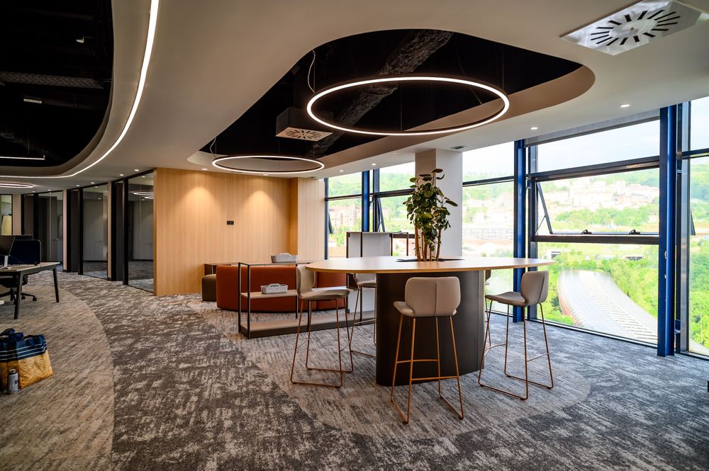 Zona informal con mesa alta, taburetes y ventanales con vistas verdes en las oficinas de Sibelco en Bilbao