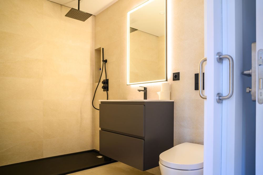 Bathroom of the home in Jaureguialde with a black shower tray, a suspended gray vanity, and a backlit mirror