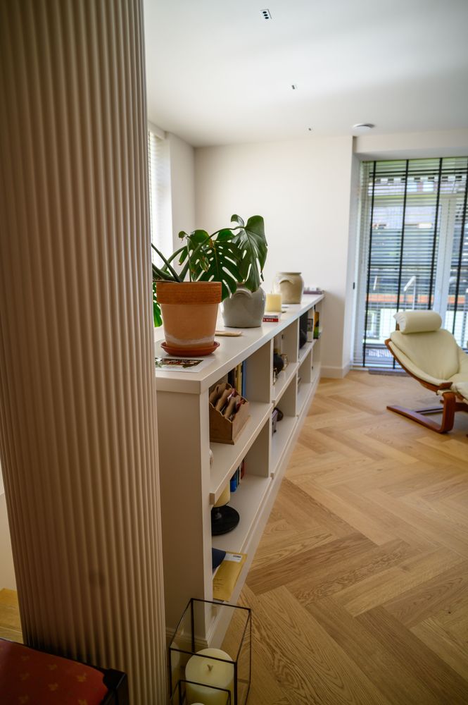 Low shelving with plants and herringbone oak flooring in the living room of the renovated home in Neguri