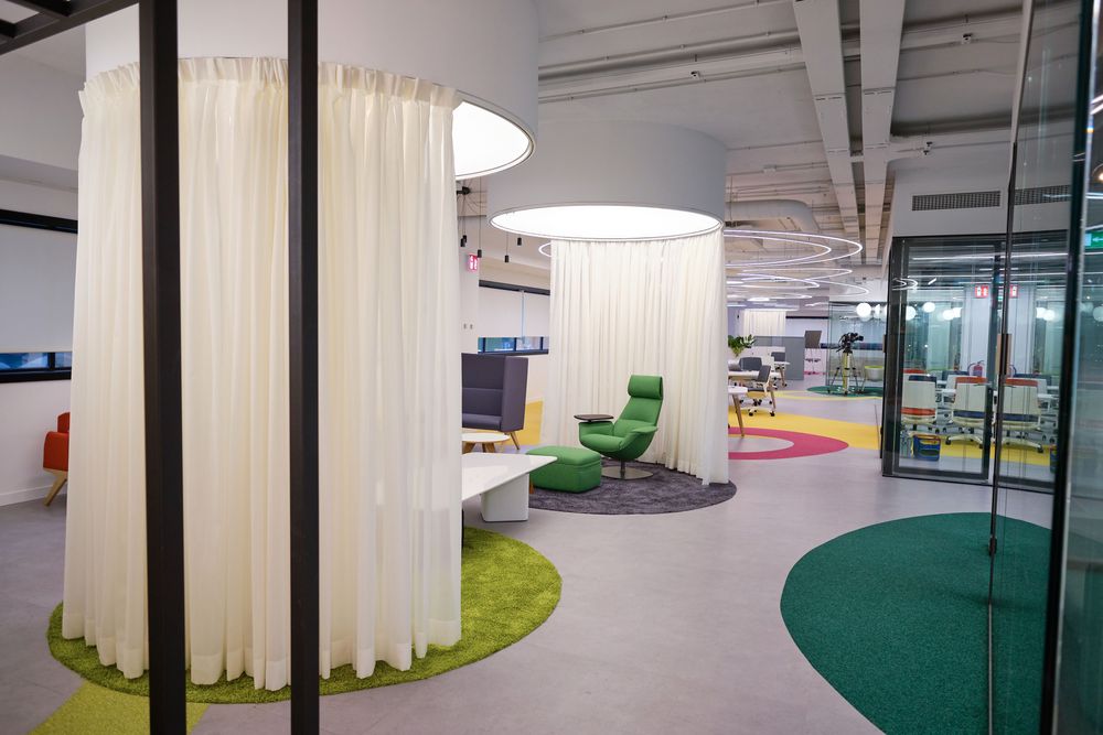 Circular booths with white curtains and a green armchair on a carpet of colorful circles at the Smartgrid Innovation Hub